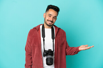 Young photographer caucasian man isolated on blue background presenting an idea while looking...