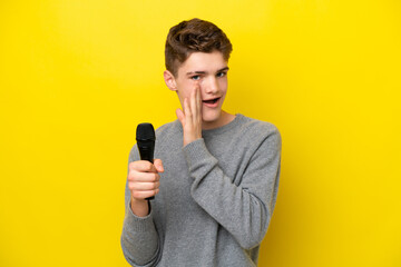 Singer Teenager man picking up a microphone isolated on yellow background whispering something