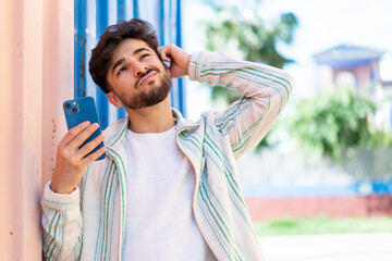 Handsome Arab man using mobile phone at outdoors having doubts and with confuse face expression