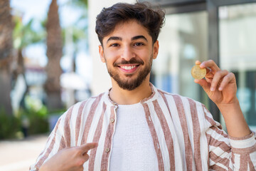 Handsome Arab man holding a Bitcoin at outdoors with surprise facial expression
