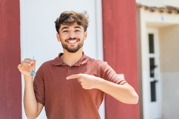 Young Arabian handsome man holding home keys at outdoors and pointing it