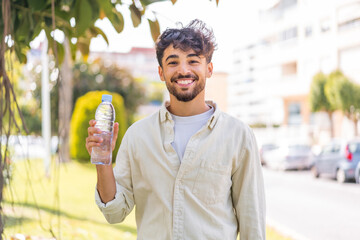 Young Arabian handsome man with a bottle of water at outdoors smiling a lot