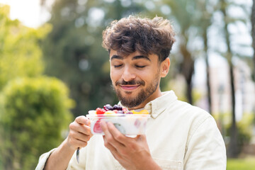 Young Arabian handsome man holding a bowl of fruit at outdoors