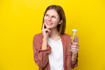 Young English woman with a bottle of water isolated on yellow background thinking an idea while looking up - obrazy, fototapety, plakaty