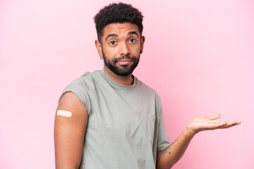 Young Brazilian man wearing a band aid isolated on pink background making doubts gesture while lifting the shoulders