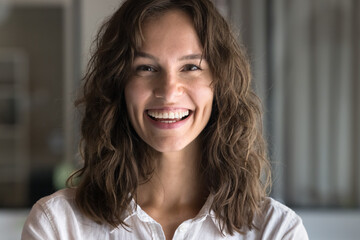Happy attractive young Caucasian woman with wavy hair looking at camera with toothy smile, laughing, posing for front close up portrait. Cheerful successful professional girl video call head shot