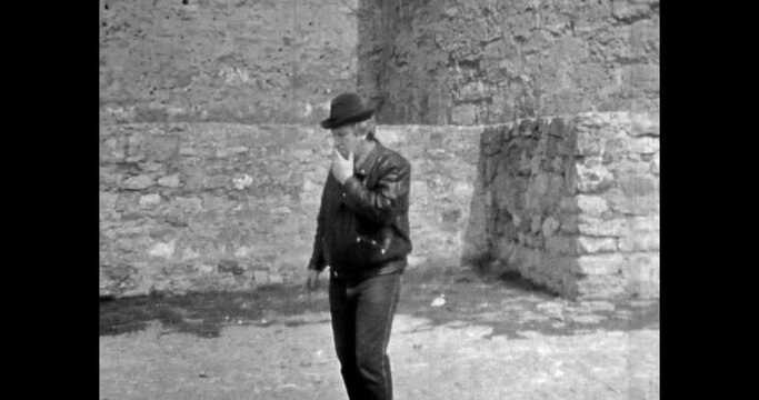 Stylish adult man lighting cigarette on city street. Man in hat, leather jacket smoking cigarette. Harmful, bad health habit. Archival vintage black white film. Old retro archive. 1980s Crimea