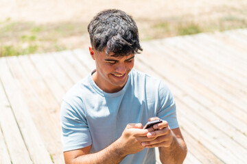 Young hispanic man at outdoors sending a message with the mobile