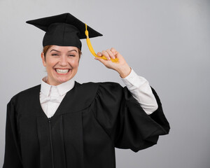 Smiling woman in graduation gown holding cap by tassel on white background. 