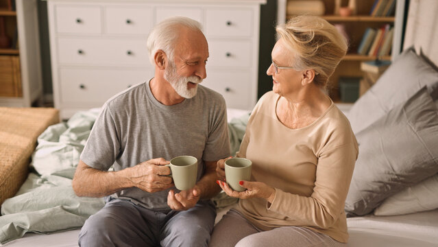Happy elderly couple enjoying coffee or tea in bed