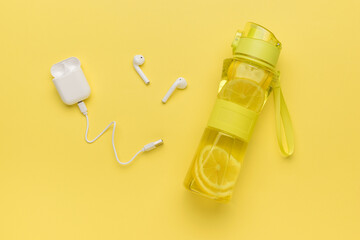 White wireless headphones and a bottle with a refreshing drink on a yellow background.
