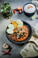 Hot plate Shell or Sambal Gami Kerang is Traditional food from Indonesia. Served on plate with a bowl of rice and vegetables top view. Super hot and spicy food