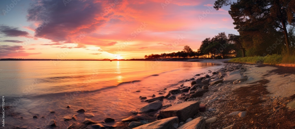 Poster scenic view of a peaceful beach with an assortment of rocks and trees under the warm hues of the set
