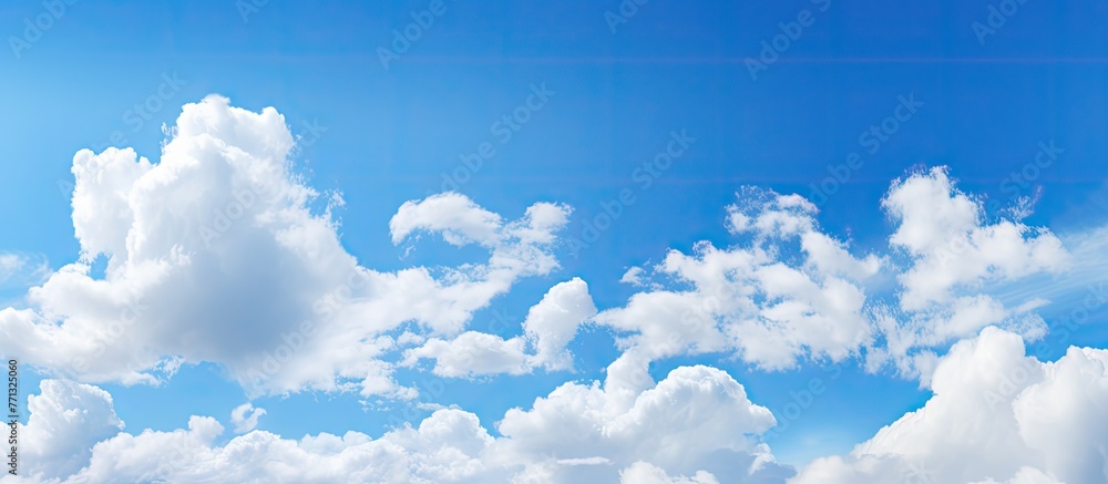 Poster white fluffy clouds are scattered across the clear blue sky above calm waters, creating a serene and
