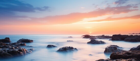 Obraz premium The mesmerizing view of the setting sun casting a warm glow over the tranquil ocean, illuminating the rocky formations and water below