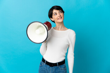 Woman with short hair isolated on blue background holding a megaphone and looking up while smiling