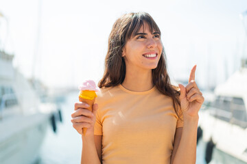 Young woman with a cornet ice cream at outdoors intending to realizes the solution while lifting a finger up - obrazy, fototapety, plakaty