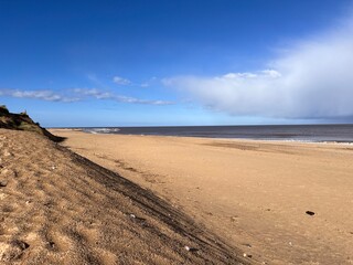 Beautiful landscape view of the vast sandy beach in Norfolk East Anglia uk with clear blue skies white cloud storm approaching calm rolling waves of sea and no people