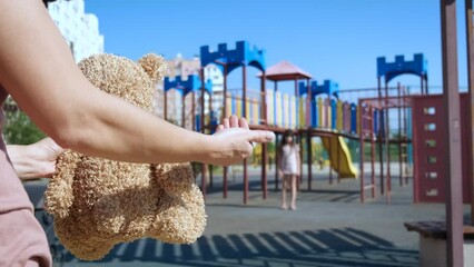 Missing children&#x27;s day on playground. A child look at the nice teddy bear in the hands of strange person. A concept of missing children&#x27;s day in the world.