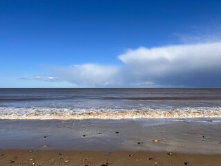 Beautiful landscape view of the vast sandy beach in Norfolk East Anglia uk with clear blue skies white cloud storm approaching calm rolling waves of sea and no people