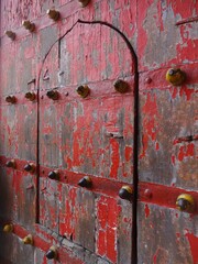 An aged, weathered wooden door in a fort, painted in a faded shade of red.