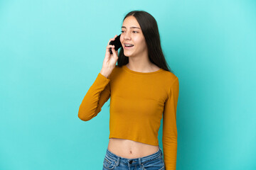 Young French woman isolated on blue background keeping a conversation with the mobile phone