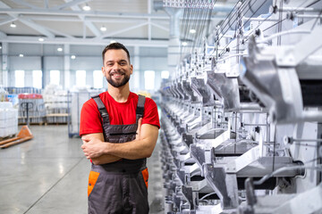 Portrait of factory worker standing by industrial machine with his arms crossed.