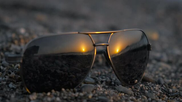 Sunglasses left on shore. A black sunglasses with ocean waves reflection on pebbles under sun rays.