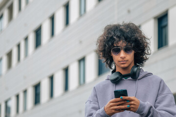 young african american man wearing headphones and playing with phone on the street