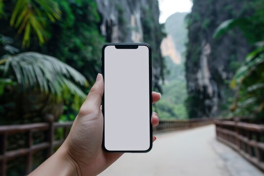 A hand holding a smartphone with a white mockup screen at a tourist attraction