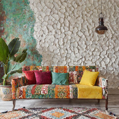 Colorful patchwork sofa against stucco wall with copy space. Eclectic, moroccan home interior design of modern living room.