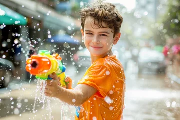 Foto op Plexiglas Happy traveler european boy wearing summer shirt holding colorful squirt water gun over blur city, Water festival holiday concept © grapestock