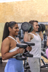 Fototapeta na wymiar Group of multiracial smiling people exercising their arms with dumbbells in a gym, sport dress, side view, vertical image. Fitness and health concept