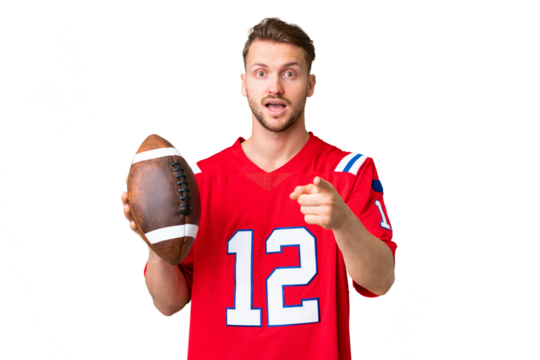 Young caucasian man playing rugby over isolated chroma key background surprised and pointing front