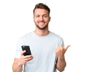 Young handsome caucasian man over isolated chroma key background using mobile phone and pointing to...