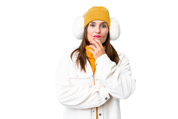 Middle age woman wearing winter muffs over isolated chroma key background having doubts and with confuse face expression