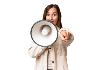 Middle-aged caucasian woman over isolated background shouting through a megaphone to announce something while pointing to the front