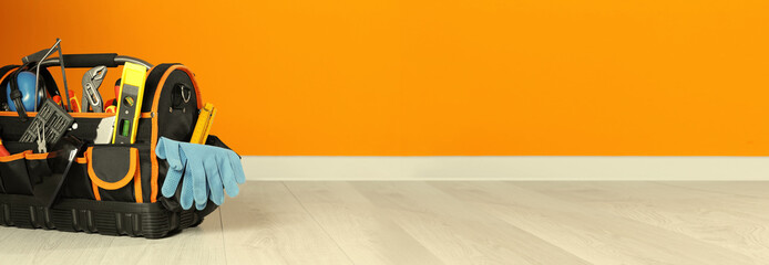 Bag with different tools for repair on floor near orange wall, space for text. Banner design