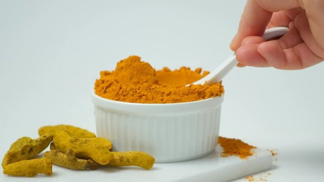Healthy turmeric spice powder in spoon macro on white background slow motion