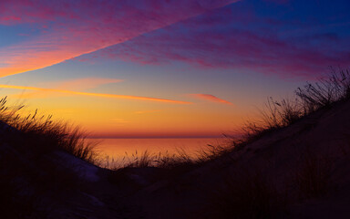 A beautiful early spring landscape of Baltic Sea beach with grass silhouettes against the colorful sky. Natural scenery of Northern Europe. - 771371475