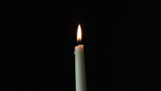 Close-up of a lit candle, light puffs move the flame until it goes out.