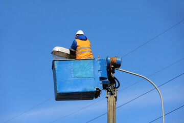 Electrician repairing the street light. Worker on the lifting platform near the lantern against the blue sky