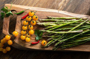 branch with yellow cherry tomatoes, asparagus, hot peppers and Brussels sprouts on a wooden board. View from above

