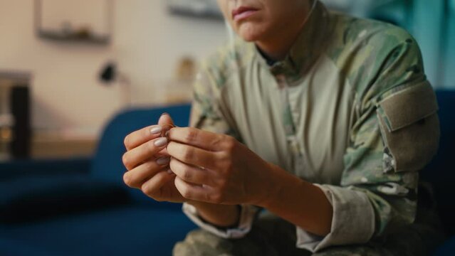 Depressed woman in military uniform holding her wedding ring, marriage problems