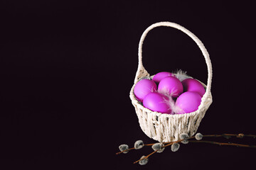 Fototapeta na wymiar Easter holiday card with basket full of pink painted eggs on black background with pussy willow twigs. Copy space. Text place. Springtime mockup design. Traditional food. Layout. Close-up