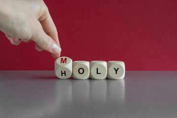 Hand turns a cube and changes the word Holy to Moly. Beautiful green background, gray table. From...