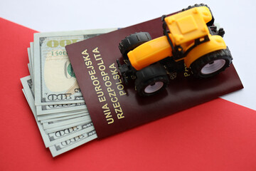 Red polish passport and yellow tractor on US money and smooth red and white flag of Poland close up - obrazy, fototapety, plakaty