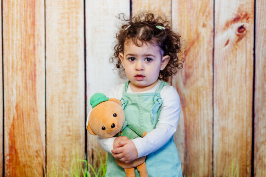 A companion in solitude. Sad little girl with curly hair holding her plushie teddy