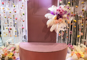 A pink wall with a decorative centerpiece that resembles a pedestal. The wall is decorated with flowers and feathers. On the sides there is a white background of curly ropes on which cosmetics hang.