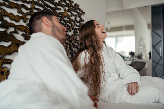 Pareja feliz andando en albornoz por hotel tomando fotos